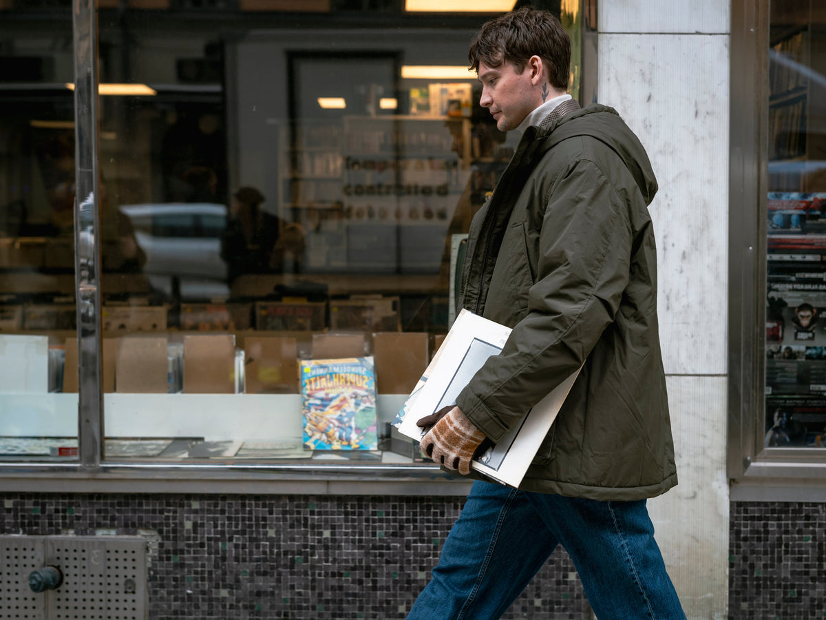 Man wearing leather gloves while walking through an urban streetscape carrying vinyl records