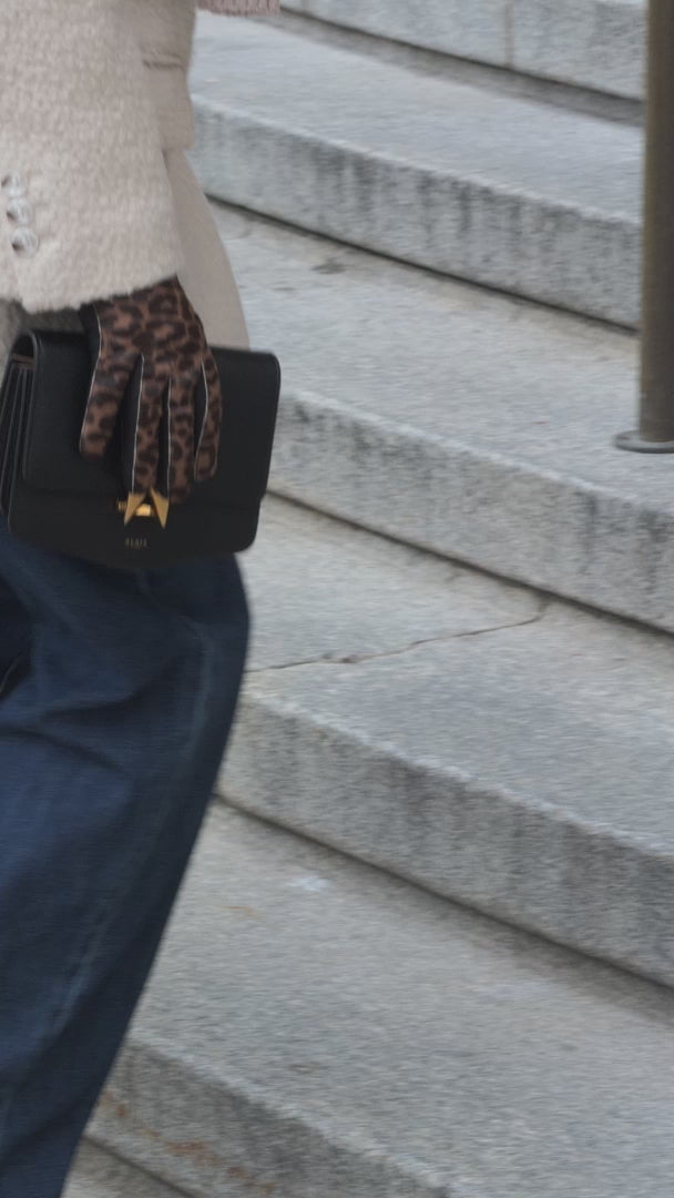 Woman wearing leopard-patterned leather gloves while holding a handbag in an urban setting.